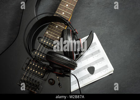 Black electric guitar and Headphone on black cement floor. Top view and copy space for text. Concept of rock music. Stock Photo