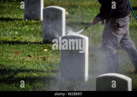 A worker at a national cemetery cleaning headstones with a pressure washer. Stock Photo