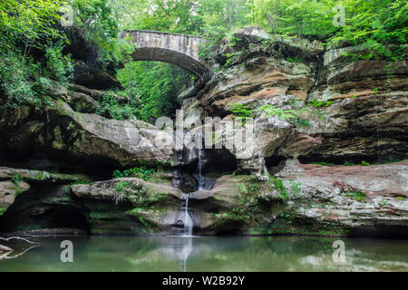 Ancient stone footbridge crosses over a ravine with a waterfall flowing into a natural lagoon. Hocking Hills State Park. Logan, Ohio. Stock Photo