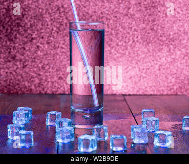 Glass of soda water and scattered ice cubes around on a wooden table Stock Photo