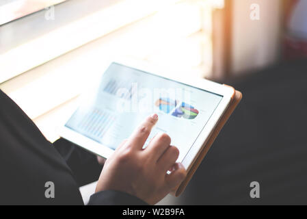 Business woman working in office with checking business report in a tablet / using a tablet computer for money analyzing graphs Stock Photo