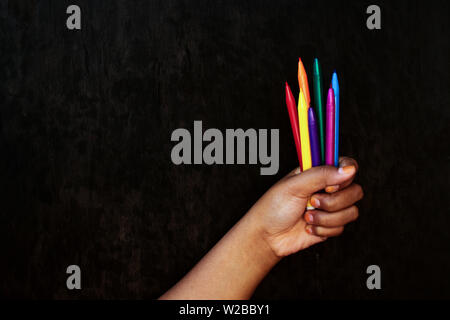 Brown Skin Girl Holding Color Markers on Black Wood Board Background Stock Photo