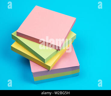stack of multicolored empty paper square stickers on a blue background, close up Stock Photo