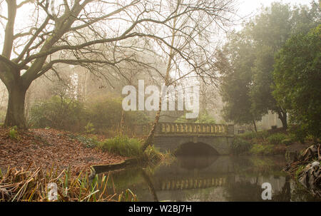 A heavy veil of fog sits over the bridge and pond in the park in late Autumn / Fall.