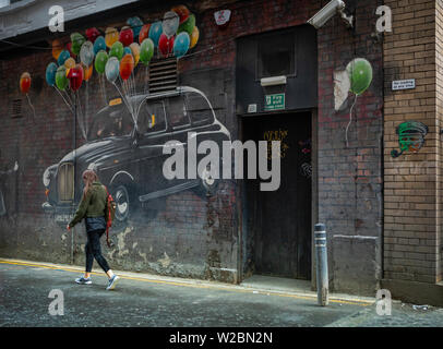 women walks in  a street in Glasgow with murals in the background Stock Photo