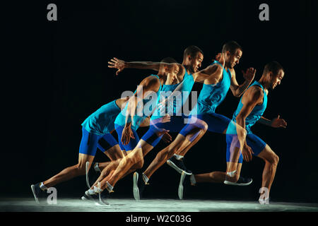 Professional male runner training isolated on black studio background in mixed light. Man in sportsuit practicing in run or jogging. Healthy lifestyle, sport, workout, motion and action concept. Stock Photo