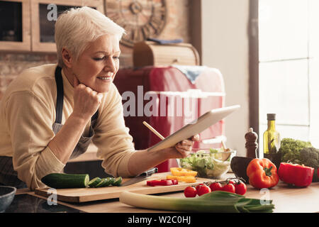 Senior lady using digital tablet at kitchen Stock Photo