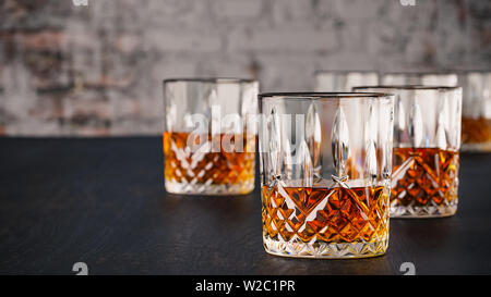 Strong alcoholic drinks, glasses and glasses, in the presence of whiskey, brandy. on a dark background of an old wooden table, shabby brick wall with Stock Photo