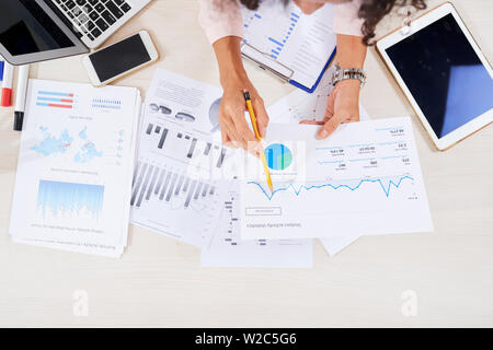 Hands of female financial manager analyzing various charts graphs and finanacial reports on her table Stock Photo