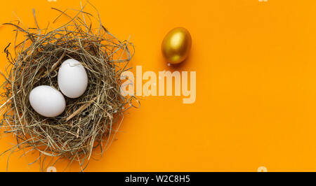 One unique golden egg standing out of two white eggs in nest Stock Photo