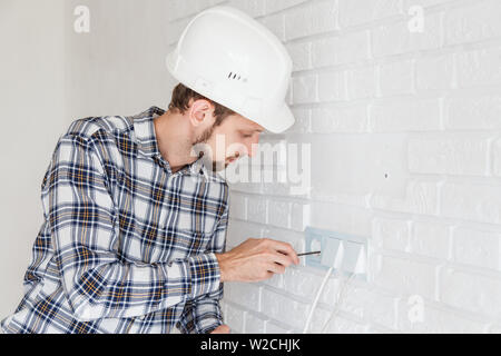 The master repairs the socket with a screwdriver installing it into the wall Stock Photo