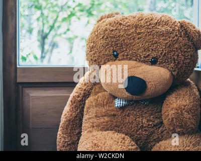Big cute teddy bear with blue plaid bow tie sitting near the wooden window glass. Stock Photo