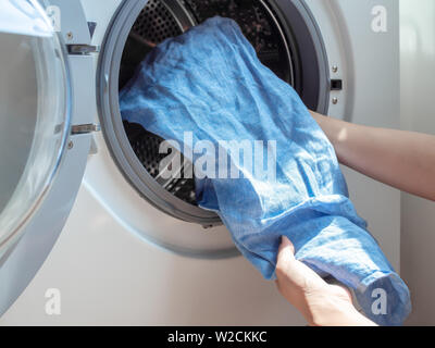 Close-up woman's hand putting dirty blue linen shirt in washing machine. Stock Photo