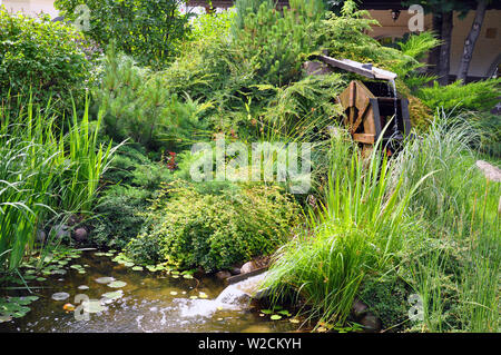 Landscape and arrangement. Driving mill wheel with falling water in the garden. Stock Photo