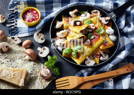 delicious Crepes with parmesan and mushrooms filling on a skillet on a concrete table with tomato sauce and kitchen towel, horizontal view from above, Stock Photo