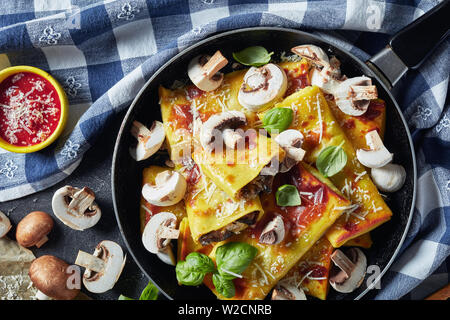 overhead view of Crepes with parmesan and mushrooms filling on a skillet on a concrete table with ingredients and kitchen towel, horizontal view from Stock Photo