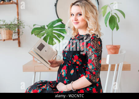 photo of pregnant woman in black dress sits and reads a book Stock Photo