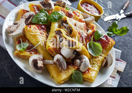close-up of Crepes with parmesan and mushrooms filling on a white plate on a concrete table with tomato sauce, view from above Stock Photo
