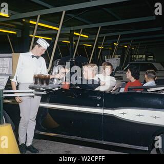 Fast food in the 1950s. Young couples in their convertible car with a at a Huddle drive-in restaurant. A waiter is serving them their order and holds his hand out to recieve the payment.  1950s 1960s ref 5-40-5 Stock Photo
