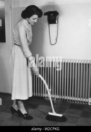 Cleaning day in the 1940s. A young woman is cleaning her apartment and is using a bush with an telescoping handle. A new invention to stand up straight when dusting and avoid back pains. Sweden 1949 Stock Photo