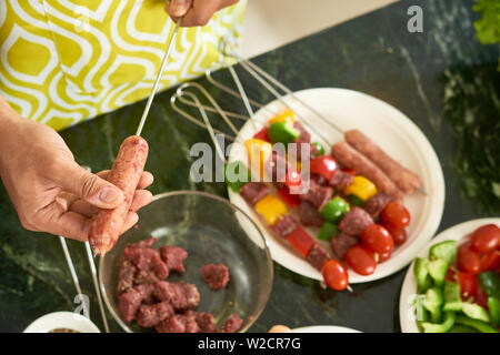 Close-up of young man cooking kebab from beef and fresh vegetables and he is going to grill it outdoors Stock Photo