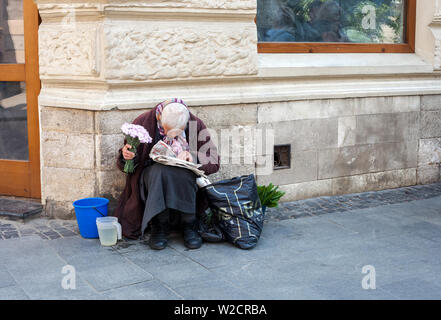 Lviv, Ukraine - 26 May 2019: Elderly woman selling flowers. Old woman sitting on street and reading newspaper Stock Photo