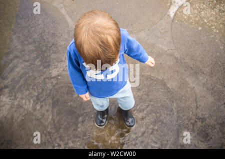 3 years boy having fun at urban puddle. High angle view Stock Photo