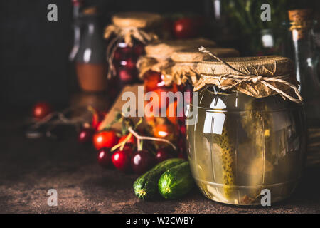 Various preserved fermented seasonal vegetables and fruits from garden in glass jars on dark rustic background, close up. Autumn canning. Conservation Stock Photo