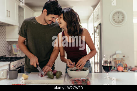 Loving young couple cutting vegetables together at kitchen counter. Young man and woman in love cooking food together at home.