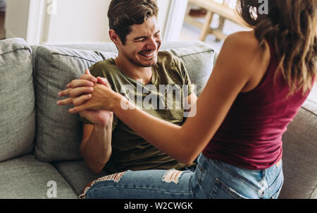 Woman sitting on top of her boyfriend on sofa. Playful couple having a fun at home. Stock Photo