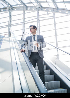 Businessman on escalator holding coffee in hand Stock Photo