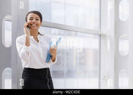 Happy african businesswoman smiling and talking on the phone, holding folder of documents Stock Photo