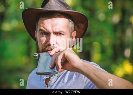 Wild West is his heart. camping and hiking. mature male with brutal look drink alcohol from flask. Bearded man in cowboy hat in park outdoor. man hipster relax in autumn forest. Spring sunny weather. Stock Photo
