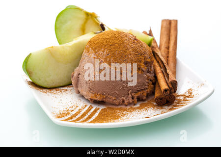ice cream sundae: a single scoop of apple cinnamon ice cream with apple slices and a cinnamon stick on a plate on white background Stock Photo