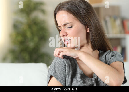 Woman suffering itching scratching shoulder sitting on a couch at home Stock Photo