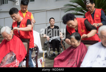 (190708) -- LINHAI, July 8, 2019 (Xinhua) -- Wu Yuanmiao (C) watches volunteers cutting hair for free at a nursing home for the aged in Linhai City, east China's Zhejiang Province, June 27, 2019. Wu Yuanmiao, when working as a barber, set a rule for himself to provide free service one day a week to the old, the disabled, and soldiers. Having served more than 60,000 customers for 17 year, he is the winner of various awards including May 1 Labor Medal. However, diagnosed with brain disease, Wu's condition has been worse off since 2008. In 2014, he experienced a hard time in running his barber Stock Photo