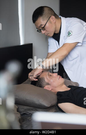 (190708) -- LINHAI, July 8, 2019 (Xinhua) -- Wu Yuanmiao receives an acupuncture therapy at home in Lucheng community of Linhai City, east China's Zhejiang Province, June 27, 2019. Doctor Hong Rong visits Wu's home every day to offer medical service. Wu Yuanmiao, when working as a barber, set a rule for himself to provide free service one day a week to the old, the disabled, and soldiers. Having served more than 60,000 customers for 17 year, he is the winner of various awards including May 1 Labor Medal. However, diagnosed with brain disease, Wu's condition has been worse off since 2008. In Stock Photo