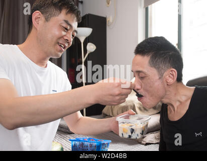 (190708) -- LINHAI, July 8, 2019 (Xinhua) -- Wu Yuanmiao (R) eats dessert with the help of his apprentice Jin Jiachun in Lucheng community of Linhai City, east China's Zhejiang Province, June 26, 2019. Wu Yuanmiao, when working as a barber, set a rule for himself to provide free service one day a week to the old, the disabled, and soldiers. Having served more than 60,000 customers for 17 year, he is the winner of various awards including May 1 Labor Medal. However, diagnosed with brain disease, Wu's condition has been worse off since 2008. In 2014, he experienced a hard time in running his Stock Photo