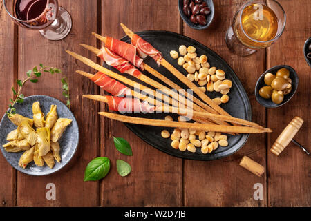 Italian antipasti, grissini with wine, parma ham, olives, and artichokes, with roasted almonds, top view Stock Photo