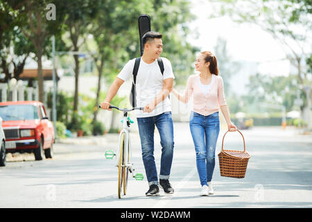 Asian young man going with bicycle and talking to his girlfriend who carrying basket they walking in the city Stock Photo