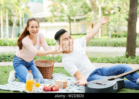Portrait of happy young Asian couple smiling at camera while having fun during their picnic in the park Stock Photo