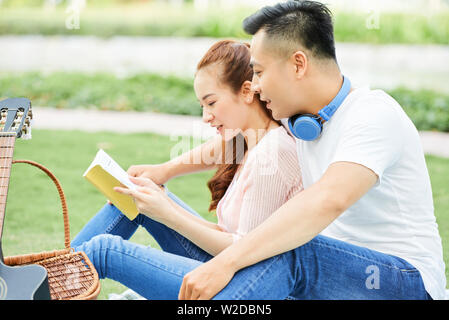 Asian young couple sitting together outdoors in the park and reading a book Stock Photo