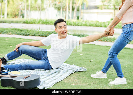 Young woman helping the young man to stand up and go after picnic in the park Stock Photo