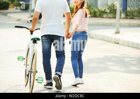 Rear view of young Asian couple with bicycle walking along the street together and holding hands Stock Photo