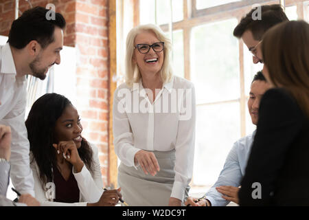 Happy multicultural young employees with old mentor laughing working together Stock Photo