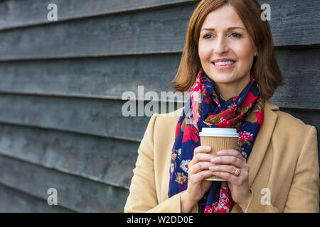 Portrait shot of an attractive, successful and happy middle aged woman female outside drinking coffee in a disposable takeaway cup. Stock Photo