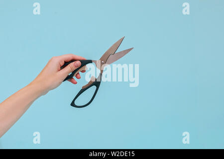 Woman's hand holding the scissors on blue background. Stock Photo