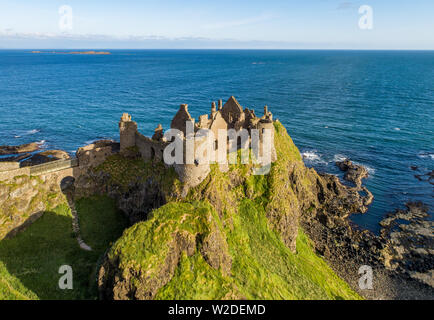 Ruins of medieval Dunluce Castle on a steep cliff. Northern coast of County Antrim, Northern Ireland, UK. Aerial view in sunrise light Stock Photo