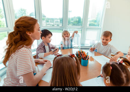 Delighted positive girl showing her drawing to the teacher Stock Photo