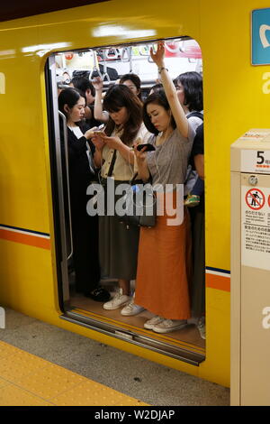 People using smart phones on a crowded Ginza Line subway train about to depart from the platform of Nihonbashi Metro station. (June 2019) Stock Photo